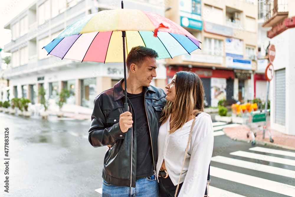 Young couple smiling happy holding umbrella standing at the city.