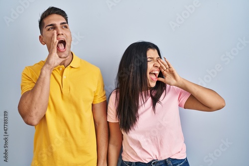 Young couple standing over isolated background shouting and screaming loud to side with hand on mouth. communication concept.