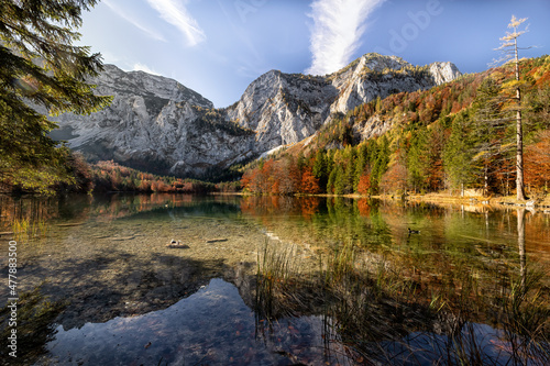 An amazing autumn scenery from Austrian Alps. Beautifully colored trees, blue sky, mountain top and all this mirrored in crystal clear lake. Breathtaking view. Travelling, exploring, relaxing.