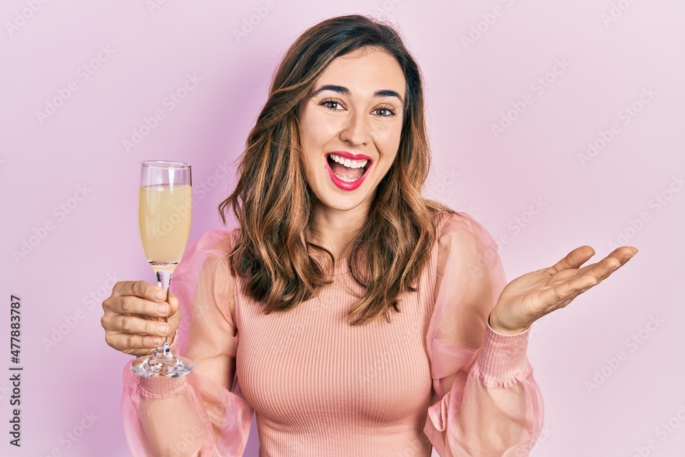 Young hispanic girl drinking a glass of sparkling champagne celebrating achievement with happy smile and winner expression with raised hand Young hispanic girl drinking a glass of sparkling champagne celebrating achievement with happy smile and winner expression with raised hand
