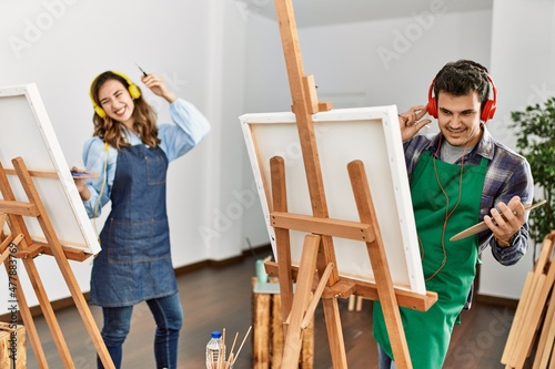 Two hispanic students smiling happy painting at art school. Standing and dancing with smile on face.