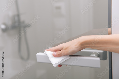 Cleaning glass door handles with an antiseptic wet wipe. Sanitize surfaces prevention in hospital and public spaces against corona virus. Woman hand using towel for cleaning home room door link.