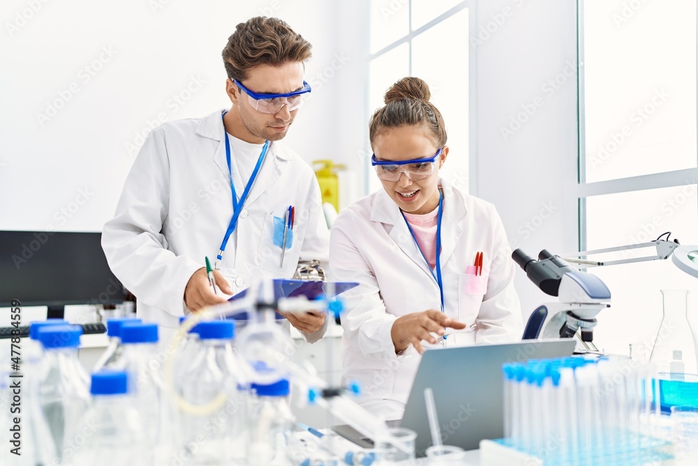 Man and woman wearing scientist uniform using laptop working at laboratory Man and woman wearing scientist uniform using laptop working at laboratory