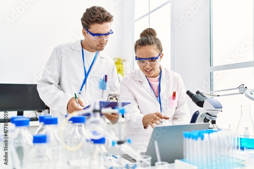 Man and woman wearing scientist uniform using laptop working at laboratory