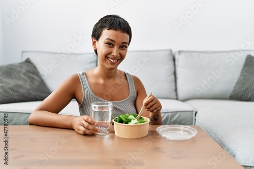 Young hispanic woman smiling confident eating salad at home