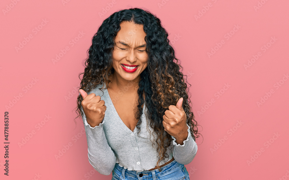 Young hispanic woman with curly hair wearing casual clothes excited for success with arms raised and eyes closed celebrating victory smiling. winner concept. Young hispanic woman with curly hair wearing casual clothes excited for success with arms raised and eyes closed celebrating victory smiling. winner concept.