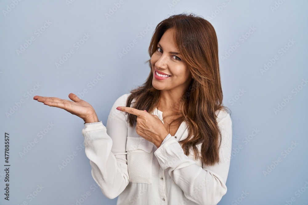 Hispanic woman standing over isolated background amazed and smiling to the camera while presenting with hand and pointing with finger. Hispanic woman standing over isolated background amazed and smiling to the camera while presenting with hand and pointing with finger.
