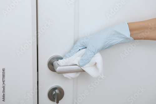 Cleaning black door handles with an antiseptic wet wipe in blue gloves. Sanitize surfaces prevention in hospital and public spaces against corona virus. Woman hand using towel for cleaning.