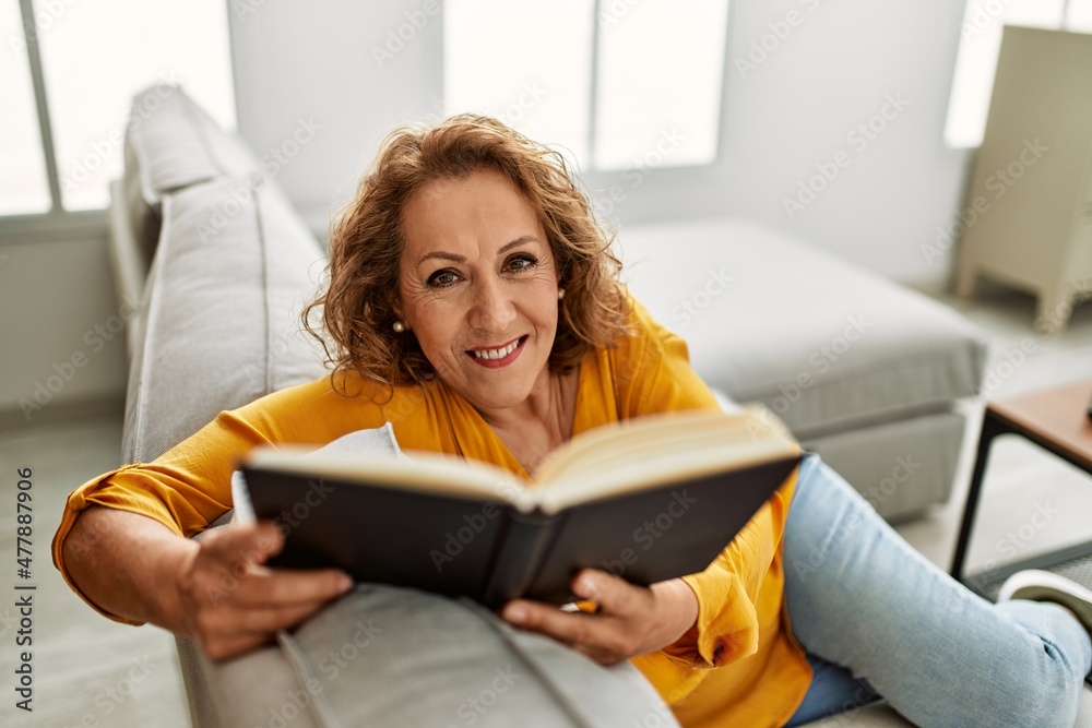 Middle age caucasian woman reading book sitting on the sofa at home. Middle age caucasian woman reading book sitting on the sofa at home.