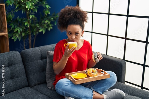 Young african american woman having breakfast sitting on sofa at home