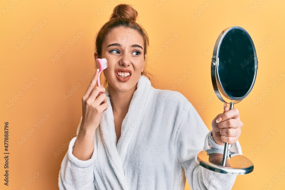 Young blonde woman wearing robe holding makeup remover brush clueless and confused expression. doubt concept. Young blonde woman wearing robe holding makeup remover brush clueless and confused expression. doubt concept.