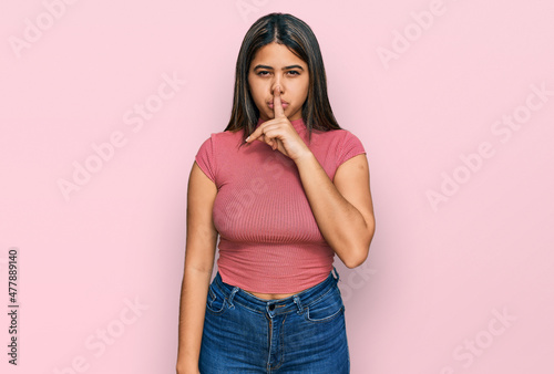 Young hispanic girl wearing casual t shirt asking to be quiet with finger on lips. silence and secret concept.