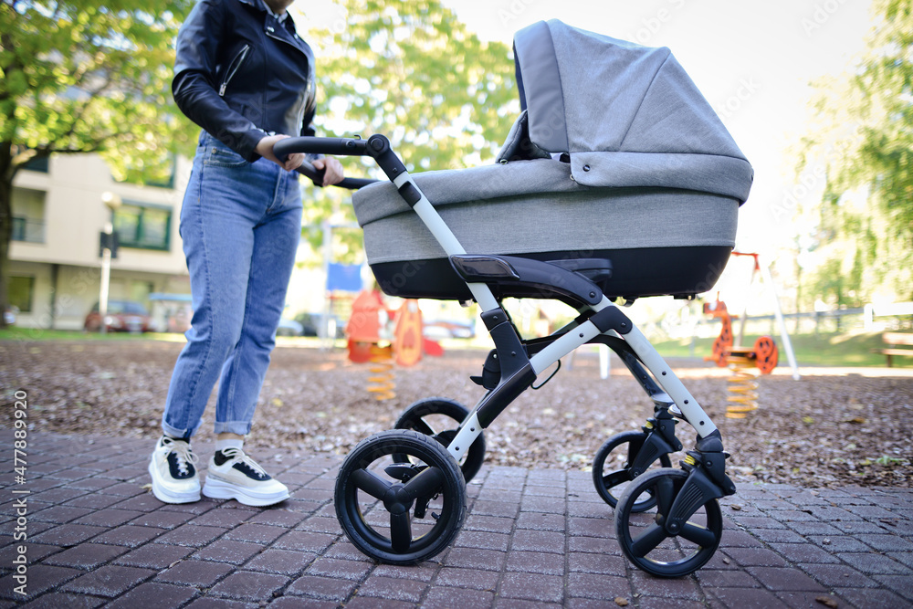 Obraz premium Woman with baby stroller walks in the park. Daily outside walking. Infant sleeping and breathing fresh air in summer.