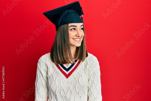 Young brunette girl wearing graduation cap looking away to side with smile on face, natural expression. laughing confident.