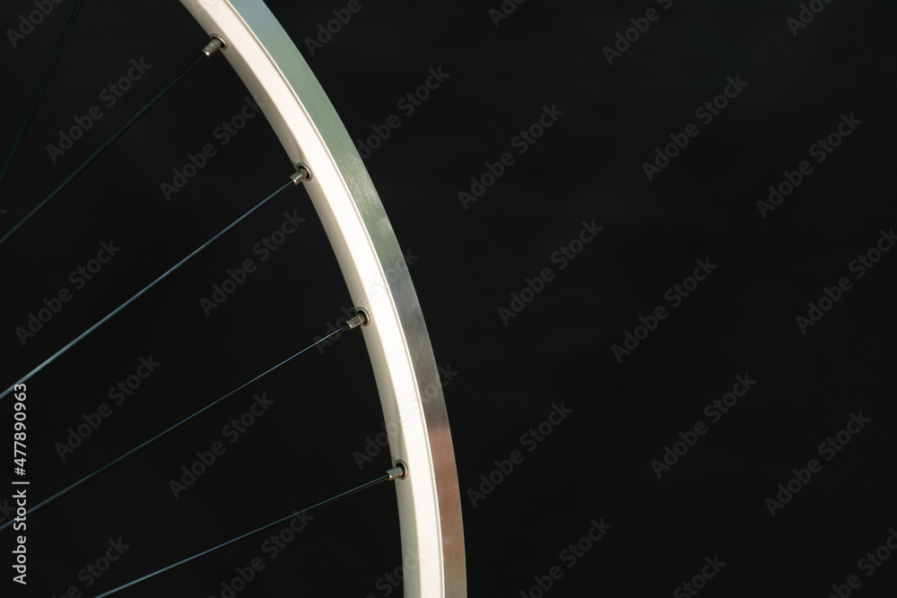 Obraz premium A bicycle wheel without a tire on a black background in the workshop. Bicycle repair. Rim and spokes of a mountain bike wheel close-up.