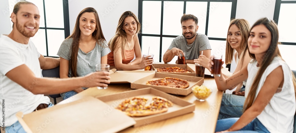 Group of young people smiling happy eating italian pizza sitting on the table at home Group of young people smiling happy eating italian pizza sitting on the table at home