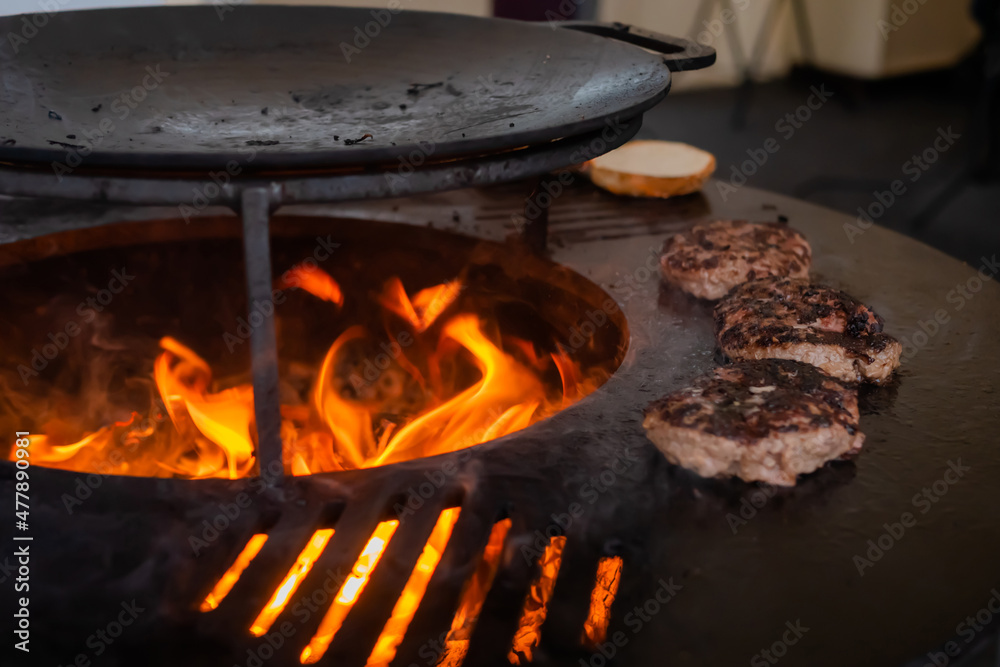 Process of grilling fresh meat cutlets for burgers on brazier with hot flame at summer local food market - close up view. Outdoor cooking, gastronomy, cookery, street food concept Process of grilling fresh meat cutlets for burgers on brazier with hot flame at summer local food market - close up view. Outdoor cooking, gastronomy, cookery, street food concept