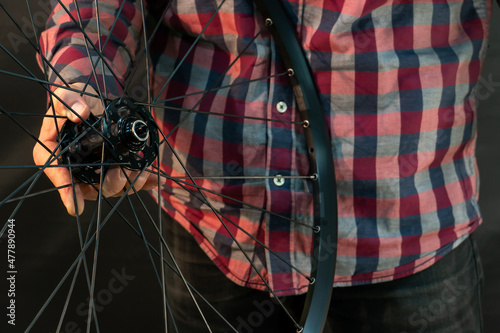 A bicycle mechanic in a shirt holds a broken wheel in his hand. Modern professional mountain bike wheel close-up on a black background.