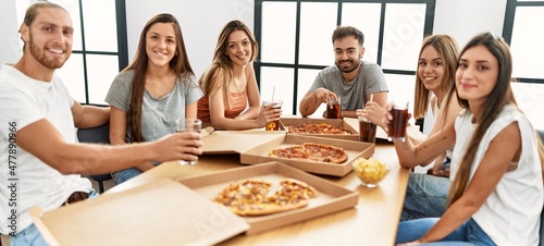 Group of young people smiling happy eating italian pizza sitting on the table at home © Krakenimages.com