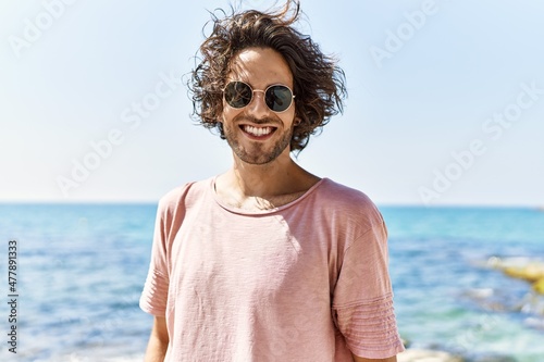 Young hispanic man smiling happy standing at the beach.