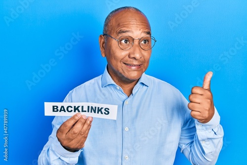 Middle age latin man holding paper with backlinks message pointing thumb up to the side smiling happy with open mouth photo