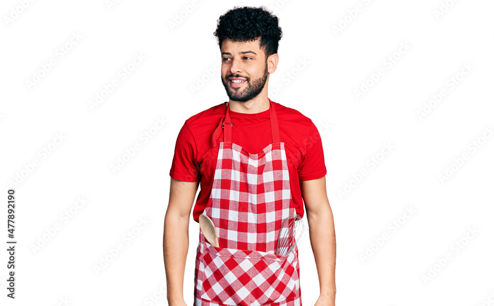 Young arab man with beard wearing cook apron looking away to side with smile on face, natural expression. laughing confident. Young arab man with beard wearing cook apron looking away to side with smile on face, natural expression. laughing confident.