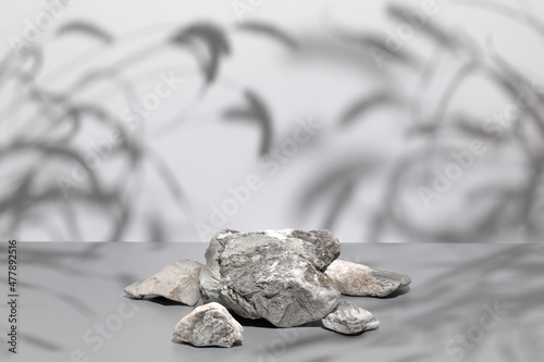 Abstract minimal nature scene - empty stage and composition of stones on gray background and soft shadows of grass and leaves. Pedestal for cosmetic product and packaging mockups display presentation