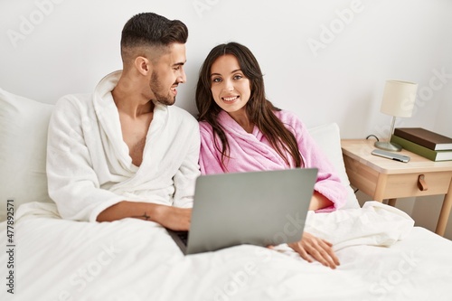 Young hispanic couple using laptop lying in bed at home.