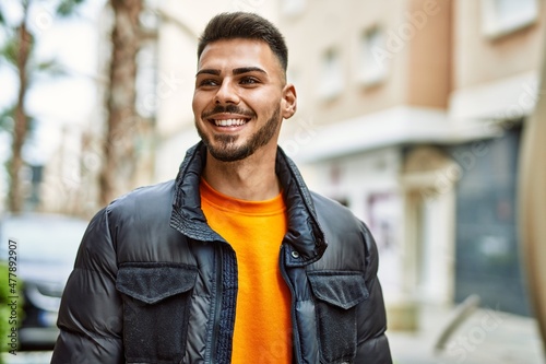 Handsome hispanic man with beard smiling happy and confident at the city wearing winter coat