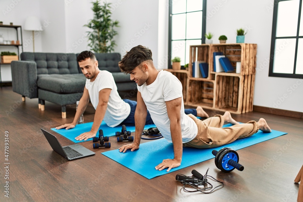 Two hispanic men couple smiling confident having online stretching class at home Two hispanic men couple smiling confident having online stretching class at home