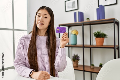Young chinese girl holding credit card sitting on the table at home.