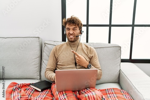 Young handsome man with beard wearing operator headset working from home pointing aside worried and nervous with forefinger, concerned and surprised expression