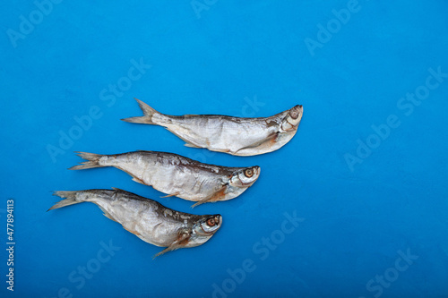 Three Sabrefish  Pelecus cultratus  on blue background. Salty dry fish - popular beer appetizer in Russia. Silver fish