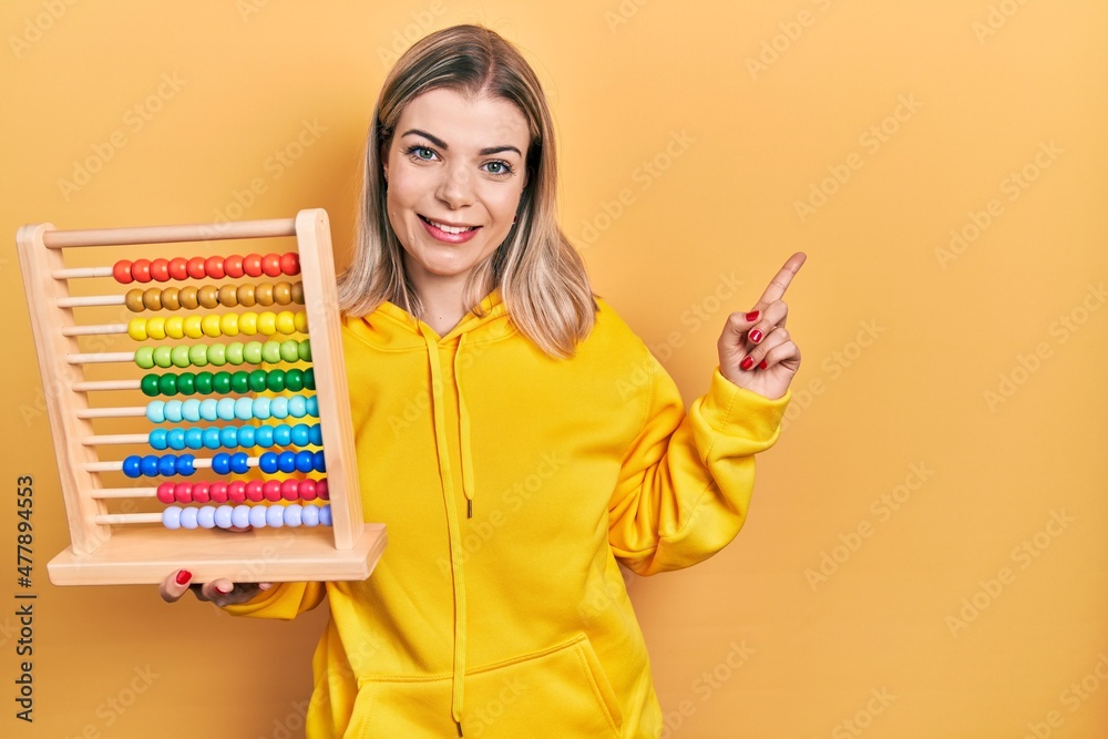 Beautiful caucasian woman holding traditional abacus smiling happy pointing with hand and finger to the side
