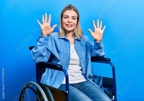 Beautiful caucasian woman sitting on wheelchair showing and pointing up with fingers number ten while smiling confident and happy.