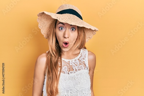 Young caucasian woman wearing summer hat afraid and shocked with surprise expression, fear and excited face.