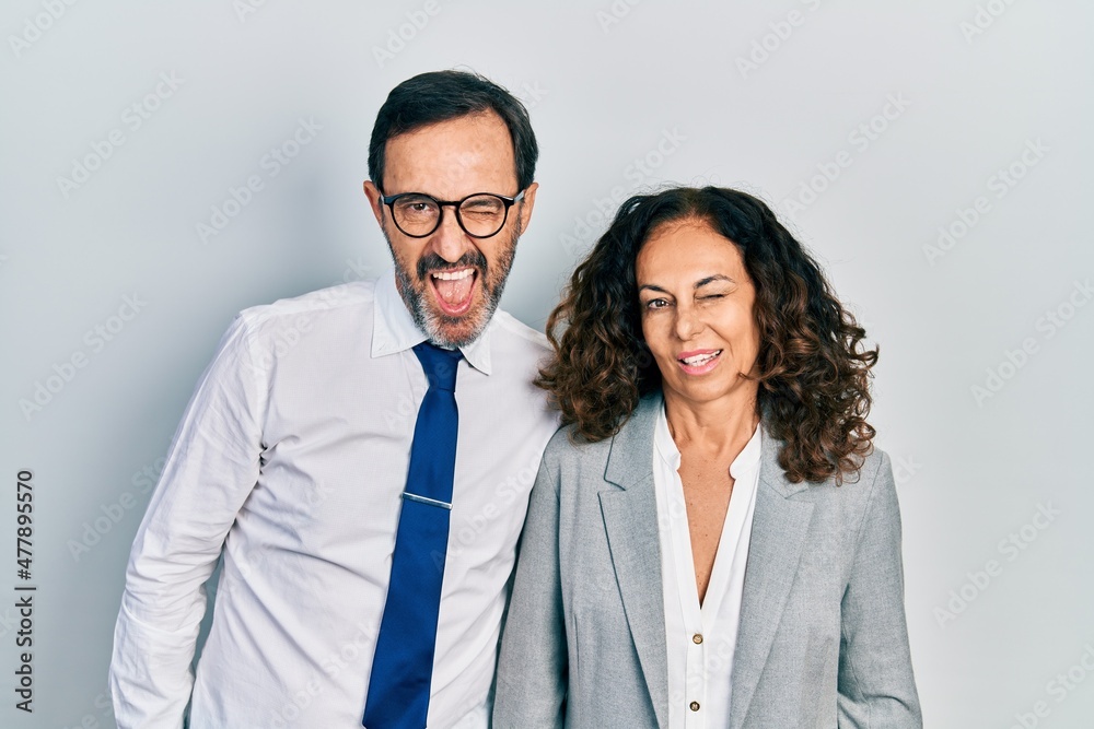 Middle age couple of hispanic woman and man wearing business office uniform winking looking at the camera with sexy expression, cheerful and happy face. Middle age couple of hispanic woman and man wearing business office uniform winking looking at the camera with sexy expression, cheerful and happy face.
