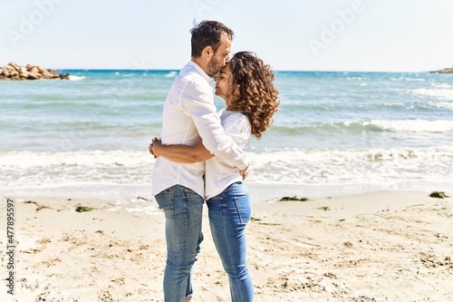 Middle age hispanic couple kissing and hugging standing at the beach.