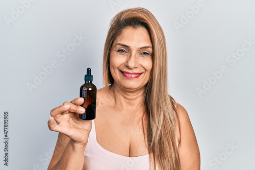 Middle age hispanic woman using night serum looking positive and happy standing and smiling with a confident smile showing teeth