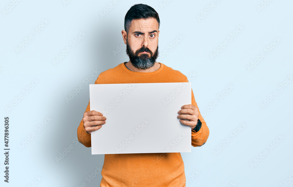 Hispanic man with beard holding blank empty banner depressed and worry for distress, crying angry and afraid. sad expression. Hispanic man with beard holding blank empty banner depressed and worry for distress, crying angry and afraid. sad expression.