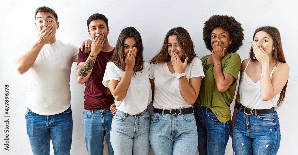 Group of young friends standing together over isolated background laughing and embarrassed giggle covering mouth with hands, gossip and scandal concept Group of young friends standing together over isolated background laughing and embarrassed giggle covering mouth with hands, gossip and scandal concept
