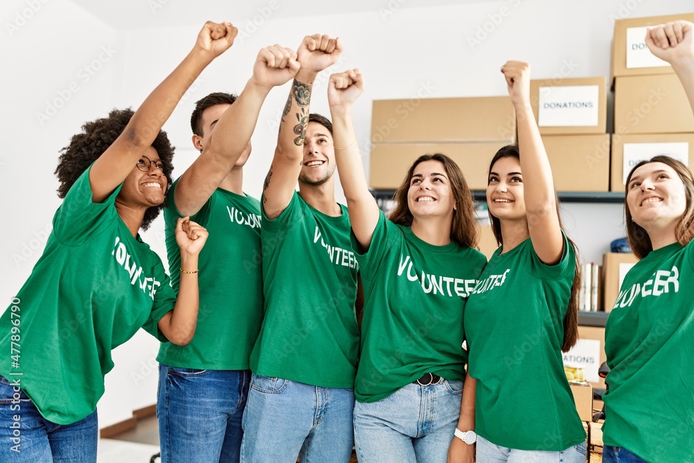 Obraz premium Group of young volunteers smiing happy with fists raised up at charity center.
