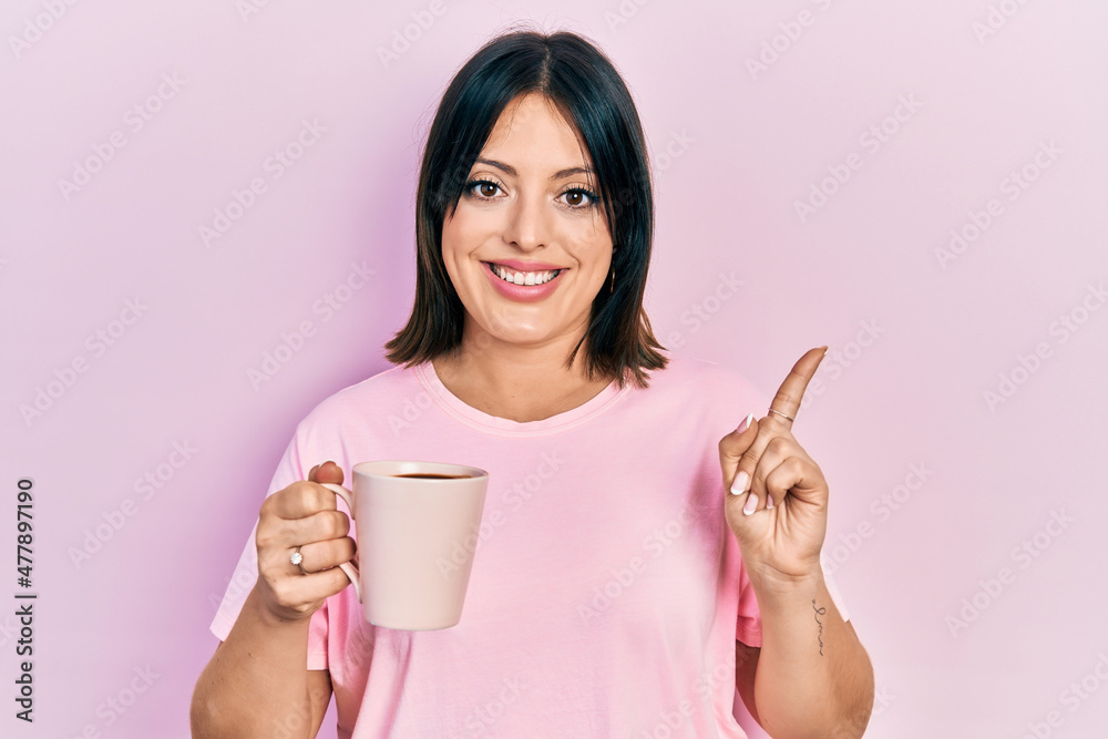 Young hispanic woman drinking a cup of coffee smiling happy pointing with hand and finger to the side Young hispanic woman drinking a cup of coffee smiling happy pointing with hand and finger to the side