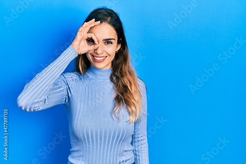 Young hispanic girl wearing casual clothes doing ok gesture with hand smiling, eye looking through fingers with happy face.