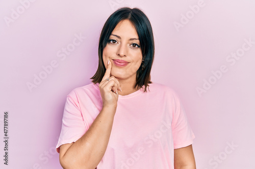 Young hispanic woman wearing casual pink t shirt looking confident at the camera with smile with crossed arms and hand raised on chin. thinking positive. © Krakenimages.com