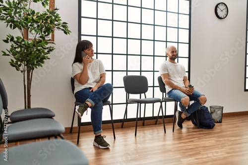 Two hispanic person boring talking on the smartphone at waiting room.