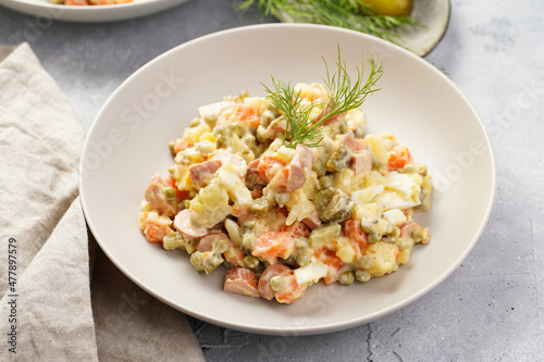 traditional east european dish for New Year's Eve - salad "Olivier" with potatoes, carrots, onion, peas, sausage, cucumbers, eggs and mayonnaise in a grey bowl