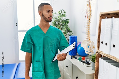 African american physiotherapist man working at pain recovery clinic looking to side  relax profile pose with natural face and confident smile.