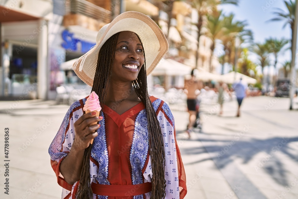 Young african american woman wearing summer hat and eating ice cream at the city.
