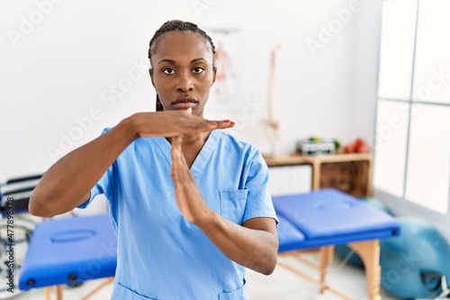 Black woman with braids working at pain recovery clinic doing time out gesture with hands, frustrated and serious face